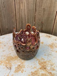 a brown and pink vase sitting on top of a white table next to a wooden fence