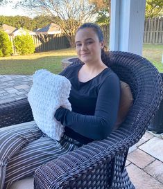 a woman sitting in a wicker chair holding a knitted white and black pillow