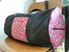 a pink and black duffel bag sitting on top of a wooden table next to a chair