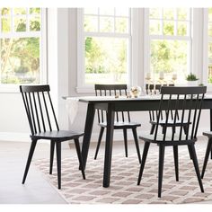 a dining room table with four chairs and a rug on the floor in front of it