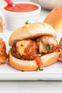 two meatball sub sandwiches on a plate with dipping sauces and bread rolls in the background