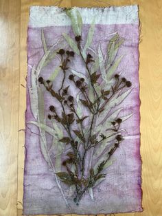 a piece of cloth with some plants on it sitting on a wooden floor next to a table