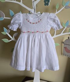 This dress is hand smocked in white.  Dainty embroidery around the front neckline and waist of the dress. Dress is fully lined with soft cotton material. The back closes with a zip and tie sashes.  This dress id made out of soft cotton fabric and lined in cotton fabric too. Suitable for kids with sensitive skin. 100% Cotton fabric Cold gentle machine wash Size 3-6 months (AU 00) Length 14" Chest circumference 20" Size 6-12 months (AU 0) Length 16" Chest circumference 21" Size 1  (12-18 months) Length 18" Chest circumference 22" Size 2 (18-24 months) Length 20" Chest circumference 23" Size 3 Length 22"  Chest circumference 24" Size 4  Length 24"  Chest circumference 25" Size 5   Length 26"  Chest circumference 26" White Short Sleeve Dress With Smocked Back, Cotton Smocked Dress With Ruffles For Baptism, White Floral Embroidered Dress For Baptism, White Fitted Smocked Dress For Baptism, White Fitted Smocked Dress With Smocked Cuffs, Baptism Smocked Dress With Short Sleeves, Fitted Smocked Dress For Baptism In Summer, Spring Baptism Dress With Smock Detail, White Cotton Smocked Dress For Baptism