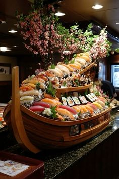 a boat filled with lots of sushi on top of a counter next to flowers