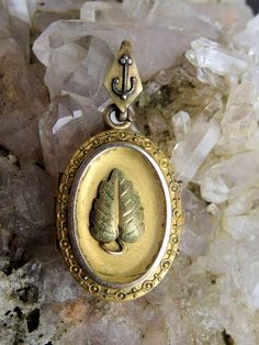 Here is a wonderful Victorian era gold fill or rolled gold plated oval locket. The piece has an applied embossed triangular shaped leaf at the center, with a green gold tint, stippled detail on the surface and a rosy gold stem. The piece is bordered by a slim gold border, with an Etruscan style wire and bead border around the outer edge. The locket is finished with a large kite shaped bail with a wire and bead anchor decorating the front, and an S-shaped soldered wire connecting the piece to the Gold Oval Heirloom Locket Necklace, Ornate Gold Oval Cabochon Jewelry, Victorian Engraved Oval Cabochon Jewelry, Heirloom Oval Jewelry For Jewelry Making, Ornate Oval Antique Gold Jewelry, Ornate Oval Jewelry In Antique Gold, Antique Gold Oval Jewelry With Intricate Design, Oval Bronze Jewelry With Intricate Design, Oval Antique Gold Jewelry With Intricate Design