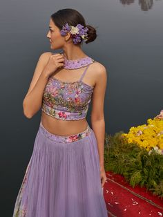 A three-piece lilac floral lehenga set from the Nikita Tiwari collection. This beautiful lilac floral pleated lehenga is paired with a printed bustier blouse. The lilac color with hand-embroidery work enhances the graceful georgette lehenga. The hand-embroidered blouse has intricate pearl-sequin details with floral print. The outfit is completed with a long floral jacket in viscos georgette material. Purple Sleeveless Wedding Set, Purple Sets With Floral Embroidery For Reception, Elegant Fitted Lavender Lehenga, Purple Floral Embroidered Set For Reception, Fitted Lavender Elegant Lehenga, Fitted Lavender Choli For Reception, Lavender Floor-length Sets For Reception, Elegant Fitted Lavender Sharara, Fitted Lavender Sharara For Reception