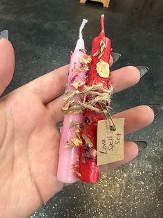 a hand holding a red candle with some tags attached to it's ends and two candles in the middle