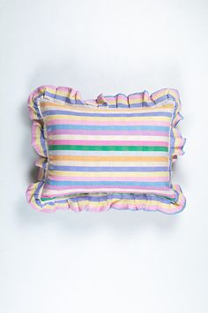 a striped pillow with ruffled edges on a white wall behind it is an orange, pink, blue and green stripe pillow