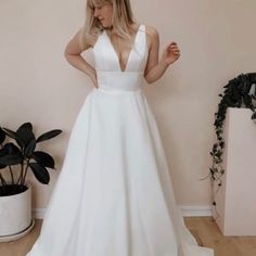 a woman in a white wedding dress standing on a wooden floor next to a potted plant