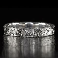 an ornate wedding band is shown on a black background, with the engraving design in white gold