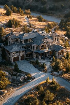 an aerial view of a large home surrounded by trees and rocks, with the driveway leading up to it