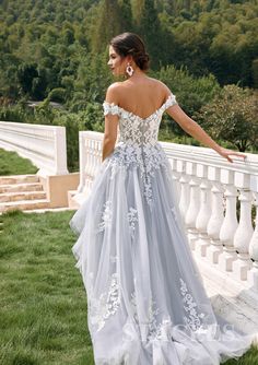 a woman in a long dress standing on the side of a white fence with her hand on her hip