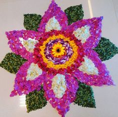 a colorful flower made out of crochet is displayed on the floor in front of a white wall