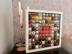 a framed bottle cap art is displayed on a table next to a pair of candles