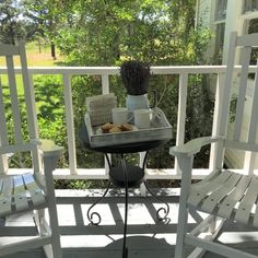 two white rocking chairs sitting on top of a porch next to a table with food