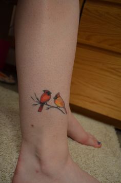 two birds sitting on a branch tattoo on the leg, with one bird perched on it's side