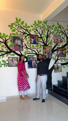 a man and woman standing in front of a tree with pictures hanging on the wall