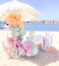 an umbrella is set up on the beach with mermaid balloons and seahorses in pastel colors