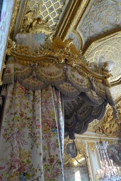 an ornate gold and white canopy bed in a room with chandeliers on the ceiling