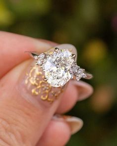 a woman's hand holding an engagement ring with two diamonds on it and gold filigrees around the band