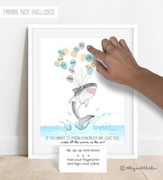 a hand holding up a framed poster with a shark and balloons floating from it's mouth