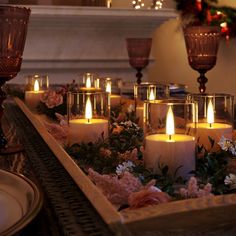 many lit candles sit in a tray with flowers and greenery on the table next to each other