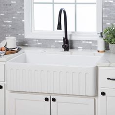 a white kitchen sink sitting under a window next to a potted plant and cutting board