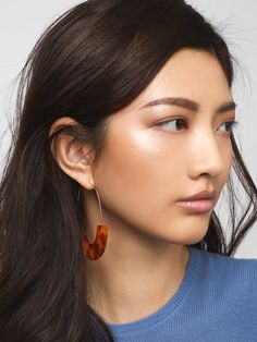 a woman with long dark hair wearing large hoop earrings in tortoise shell color