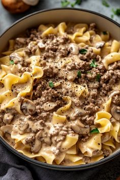 a bowl full of pasta with meat and mushrooms in sauce on the table next to garlic