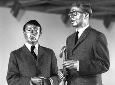 two men standing next to each other in front of a microphone and another man holding a trumpet