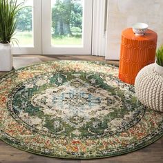 a round rug on the floor next to an orange vase and potted plant in front of a glass door