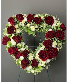 a heart shaped wreath with red and white flowers on a stand against a gray background