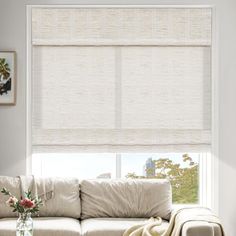 a living room with a white couch and large window covered in roman blind shades on the windowsill