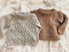 two sweaters sitting on top of a white furnishing covered bed next to each other