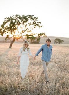 a man and woman holding hands while walking through a field