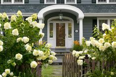 a house with white flowers in front of it and a wooden fence around the door