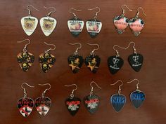 twelve guitar picks are displayed on a wooden table with metal earring clips in the shape of guitars