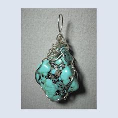 "Turquoise Nugget Pendant Wire Wrapped in .925 Sterling Silver Round Wire This inspiring stone offers a few small pebbles of golden pyrite nestled inside a light to medium turquoise-blue and black patterned background. Best worn with blue, green, coral, orange, or red; but quite versatile, and many dark, bright, pastel, and earth tone colors also wear well, especially black, grays, brown, beige/tan, and lavender. A similar color of turquoise will blend, so should be avoided. Some darker purple colors tend to clash. Take caution with yellows as well. Description: A light to bright turquoise-blue with black oxidation and very small pebbles of golden pyrite; rounded kite shaped, and opaque stone, wrapped in 22 gauge sterling silver wire. Stone Size: Medium (1-1/16\" x 7/8\" x 7/16\"). Pattern Handmade Turquoise Necklace, Wrapped Stones, Green Stone Pendant, Earth Tone Colors, Emerald Pendant, Silver Gemstone Jewelry, Bleu Turquoise, Jewelry Unique, How To Make Light