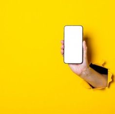 a person's hand holding a cell phone through a hole in a yellow wall