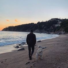 a man and his dog walking on the beach at sunset or dawn with an ocean view in the background