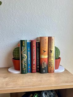 there are four books on the shelf next to a potted cacti and cactus