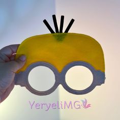 a hand holding up a yellow and black toy with glasses on it's face