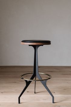 a round table with a metal base and wood top on a wooden floor in front of a gray wall