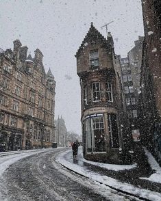 a snowy street with buildings and people walking in the snow on it's sides