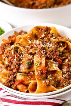 two bowls filled with pasta and meat on top of a white table next to bread