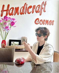 a person sitting at a table with some flowers in front of them and a sign that says handicraft corner