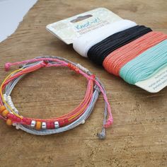 several bracelets are laying on top of a wooden table next to a roll of thread