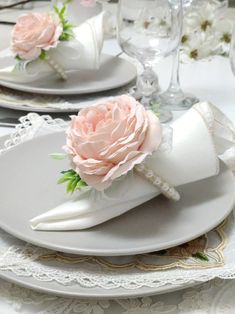 the table is set with white plates and pink flowers on them, along with lace napkins