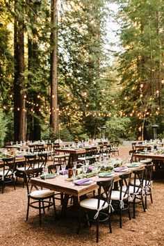 an outdoor dining area with tables and chairs set up in the woods for a wedding reception