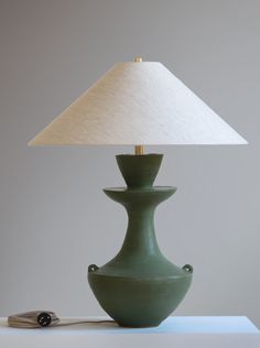 a green lamp sitting on top of a table next to a white light bulb and paper shade